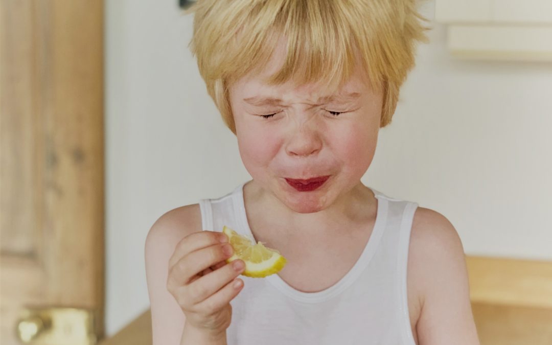 Un enfant qui grimace en goûtant une rondelle de citron très amère